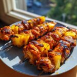 Nahaufnahme von saftigen BBQ-Hähnchen-Ananas-Spießen auf einem Teller, perfekt gegrillt.