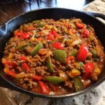 Nahaufnahme einer Cajun-Rinderpfanne mit Hackfleisch und bunten Paprikastücken in einer Gusseisenpfanne.