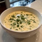 Eine Schüssel mit cremiger Blumenkohlsuppe mit Cheddar, garniert mit frischer Petersilie.