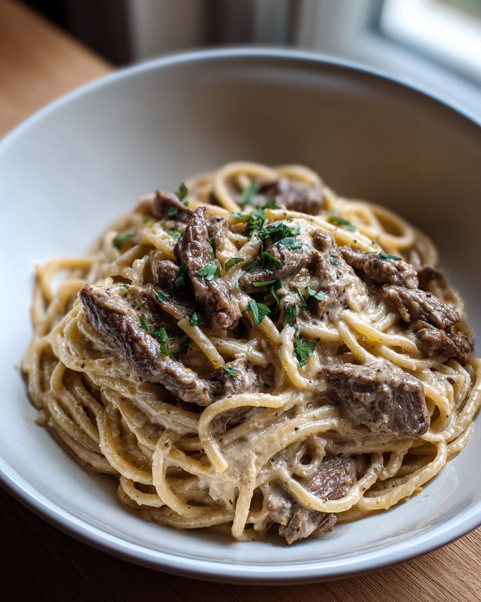 Nahaufnahme einer Schüssel mit cremiger Pilzrahm-Pasta mit zarten Rinderstreifen und frischer Petersilie.