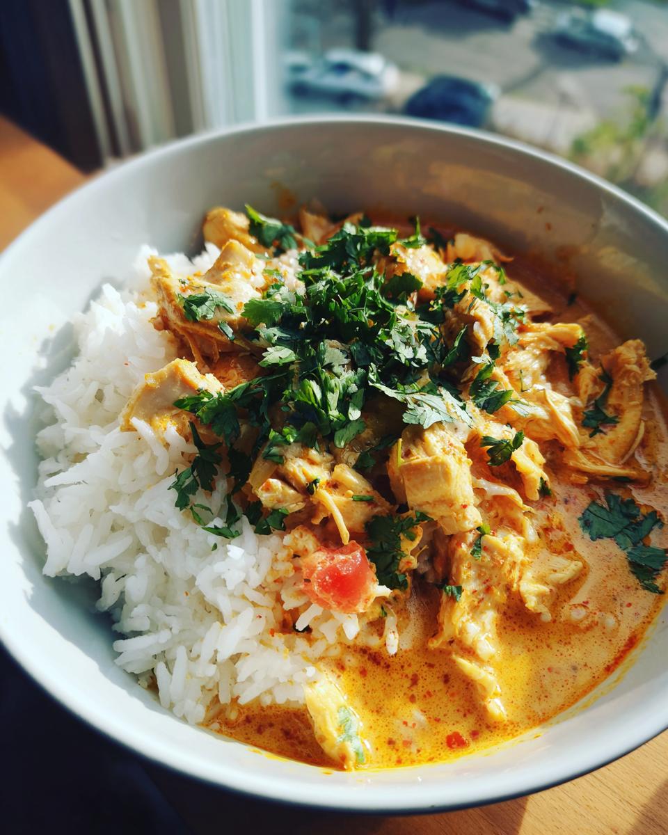 Eine Schüssel mit dampfender Curry-Kokos-Suppe mit Hähnchen und Reis, garniert mit frischer Petersilie.
