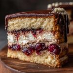 Ein saftiges Stück Donauwelle mit Buttercreme, Schokolade und Kirschen auf einem Holzbrett.