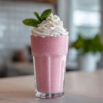 Ein cremiger Erdbeer-Milchshake mit Vanilleeis, Sahnehaube und Minze garniert.