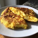 Nahaufnahme von aufgeschnittenen Frühstücks-Burritos mit Rührei und Käse auf einem weißen Teller.