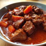 Nahaufnahme einer Schüssel mit Gulasz Wolowy, Rindergulasch nach polnischer Art, mit zarten Fleischstücken und Karotten in einer reichhaltigen Sauce.