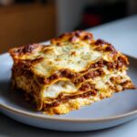Ein perfekt geschichtetes Stück hausgemachte Lasagne al Forno mit viel Käse und Bolognese auf einem Teller.