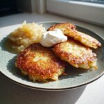 Goldbraune Kartoffelpuffer mit einem Klecks Sauerrahm und Apfelmus auf einem Teller.