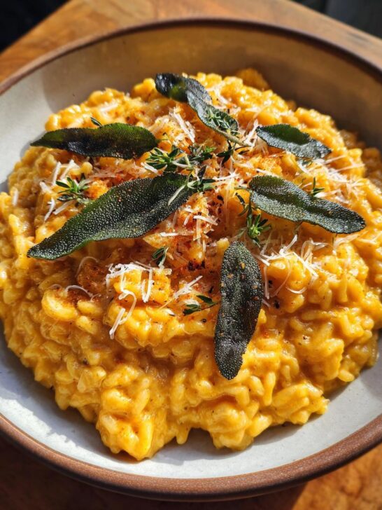 Nahaufnahme von cremigem Kürbis-Risotto mit Salbei und Parmesan, garniert mit frischen Kräutern.