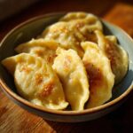 Nahaufnahme von dampfenden Pelmeni – russische Teigtaschen mit Hackfleischfüllung in einer Schüssel, bestreut mit Gewürzen.