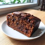 Ein saftiges Stück Schoko-Bananen-Kuchen mit vielen Schokoladenstückchen auf einem weißen Teller.