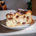 Ein Stück Sernik – Polnischer Käsekuchen mit Vanille & Rosinen, bestäubt mit Puderzucker.