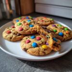 Ein Teller voller bunter Smarties Cookies, einer davon ist zerbrochen und zeigt das saftige Innere.