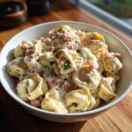 Eine Schüssel mit Tortellini in cremiger Schinken-Käse-Sauce, garniert mit Petersilie.