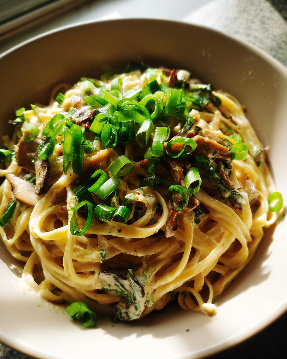Eine Schüssel mit Bandnudeln in Rahmchampignon-Sauce, garniert mit Frühlingszwiebeln.