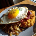 Ein Teller mit Bauern-Schnitzel mit Zwiebeln, Speck und einem perfekt gebratenen Spiegelei.