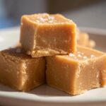 Nahaufnahme von drei gestapelten Stücken cremigem Peanut Butter Fudge, bestreut mit grobem Meersalz.
