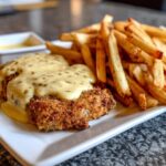 Ein goldbraunes Käse-Sahne-Schnitzel mit einer cremigen Sauce und knusprigen Pommes Frites auf einem weißen Teller.