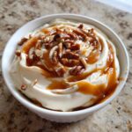 Nahaufnahme des fertigen Karamell Apfel Dip in einer weißen Schale, garniert mit Karamellsauce und gehackten Pekannüssen.