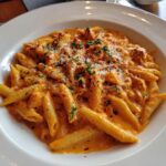 Nahaufnahme von Penne in einer cremigen Tomaten-Frischkäse-Sauce, bestreut mit Kräutern und Chili.