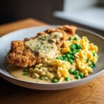 Ein Teller mit knusprigem Rahmschnitzel, cremigen Butterspätzle und leuchtend grünen Erbsen, garniert mit Petersilie.