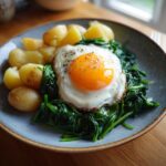 Teller mit Rahmspinat, einem Spiegelei und Salzkartoffeln, perfekt für ein schnelles Mittagessen.