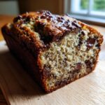 Nahaufnahme eines saftigen Banana Bread mit Chocolate Chips, das auf einem Holzbrett liegt.