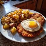Ein Teller mit Schnitzel „Holsteiner Art“, einem Spiegelei und knusprigen Bratkartoffeln, perfekt für ein herzhaftes Mittagessen.