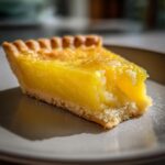 Nahaufnahme eines saftigen Stücks Tarte au Citron mit hellem Mürbeteigboden und glänzender Zitronenfüllung.