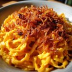 Nahaufnahme von Tagliatelle in cremiger Kürbis-Rahm-Soße, garniert mit knusprigen Röstzwiebeln.