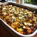 Nahaufnahme eines goldbraunen Zucchini-Kartoffel-Auflaufs mit Feta und Kräutern, frisch aus dem Ofen.