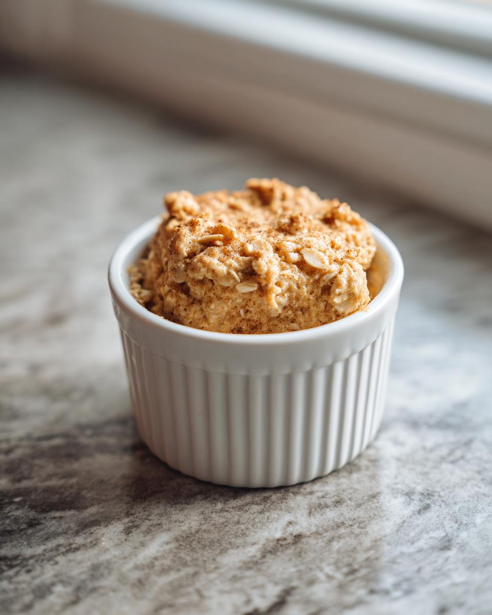 Ein einzelnes, fluffiges Baked Oats mit Eiweißpulver, bestreut mit Zimt, in einer weißen Ramekin-Form.