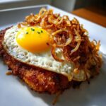 Nahaufnahme eines knusprigen Bauern-Schnitzels mit einem Spiegelei und vielen goldbraunen Röstzwiebeln.