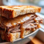 Nahaufnahme eines getoasteten Braten-Sandwich mit dick belegten Fleischscheiben und reichlich Bratensauce.