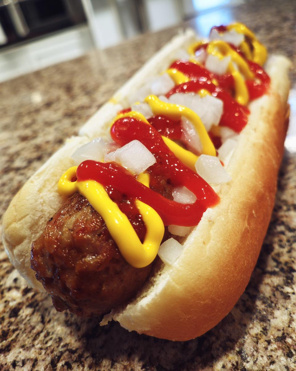 Nahaufnahme eines saftigen Bratwurst-Hotdog deutsch im Brötchen mit Ketchup, Senf und Zwiebeln.