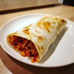 Nahaufnahme eines perfekt gerollten Chorizo-Burrito mit würziger Füllung auf einem weißen Teller.