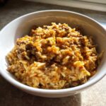 Nahaufnahme einer weißen Schale mit cremiger Paprika-Hack-Reispfanne ohne Paprikastückchen.