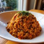 Ein Berg cremige Tomaten-Hack-Reispfanne, garniert mit frischer Petersilie, in einer weißen Schüssel.