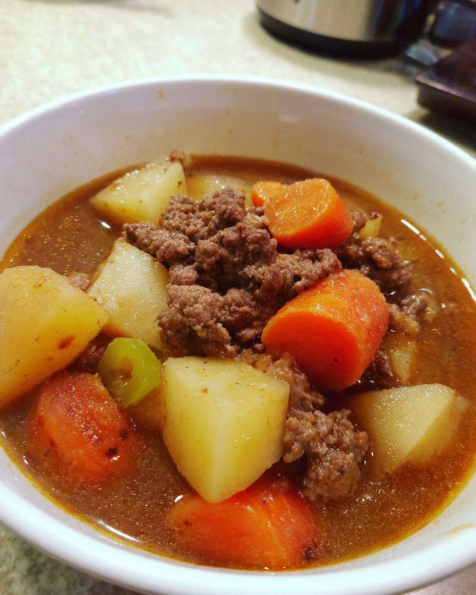 Nahaufnahme einer Schüssel mit deftigem Bauerntopf mit Hackfleisch, Kartoffelwürfeln und Karotten in würziger Soße.