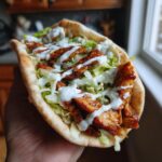 Nahaufnahme einer gefüllten Schnelle Gyros-Pita aus der Pfanne mit Fleisch, Salat und viel Soße.