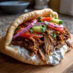 Nahaufnahme eines gefüllten Gyros-Sandwich im Fladenbrot mit Fleisch, Tzatziki und frischem Gemüse.