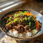 Nahaufnahme eines Korean Beef Bowl mit Rinderhack, Reis, Karottenstreifen und Frühlingszwiebeln.