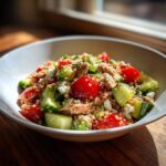 Nahaufnahme einer Mediterranen Thunfisch-Bowl mit Quinoa, Kirschtomaten, Gurkenstücken und Feta.