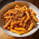 Nahaufnahme einer weißen Schüssel mit cremiger Pasta in Tomaten-Sahne-Sauce mit Hackfleisch und Kräutern.