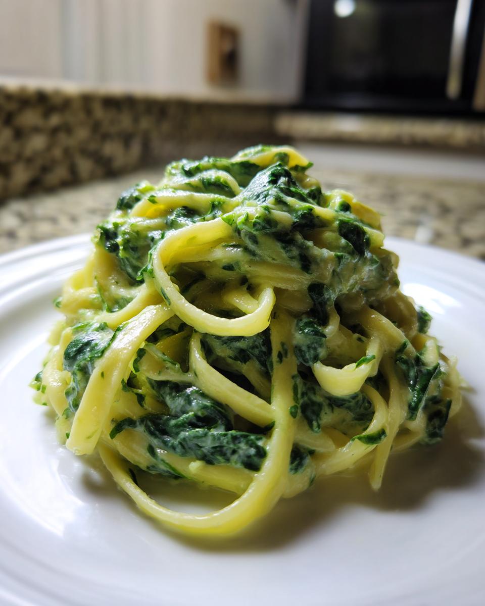 Nahaufnahme von Pasta mit Rahmspinat und Knoblauch auf einem weißen Teller, sehr cremig.