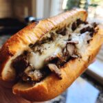 Nahaufnahme eines saftigen Philly Cheesesteak Sandwichs mit dünn geschnittenem Fleisch und geschmolzenem Käse im Brötchen.