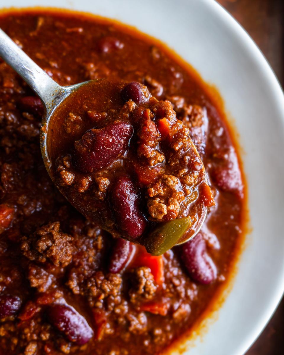 Nahaufnahme von einem Löffel voll Pikantes Chili con Carne mit Hackfleisch und Kidneybohnen in einer weißen Schüssel.