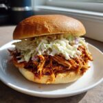 Nahaufnahme eines saftigen Pulled Chicken Sandwich mit BBQ-Sauce und cremigem Krautsalat auf einem weichen Brötchen.