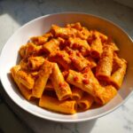 Nahaufnahme von Rigatoni in einer leuchtend orangefarbenen, cremigen Paprika-Sahnesauce in einer weißen Schüssel.