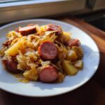 Ein Teller mit herzhaftem Sauerkraut und Kielbasa mit Kartoffeln, appetitlich angerichtet im Sonnenlicht.