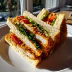 Zwei Hälften eines saftigen Schnitzel-Sandwichs mit goldbrauner Panade, Salat und Tomaten auf einem weißen Teller.